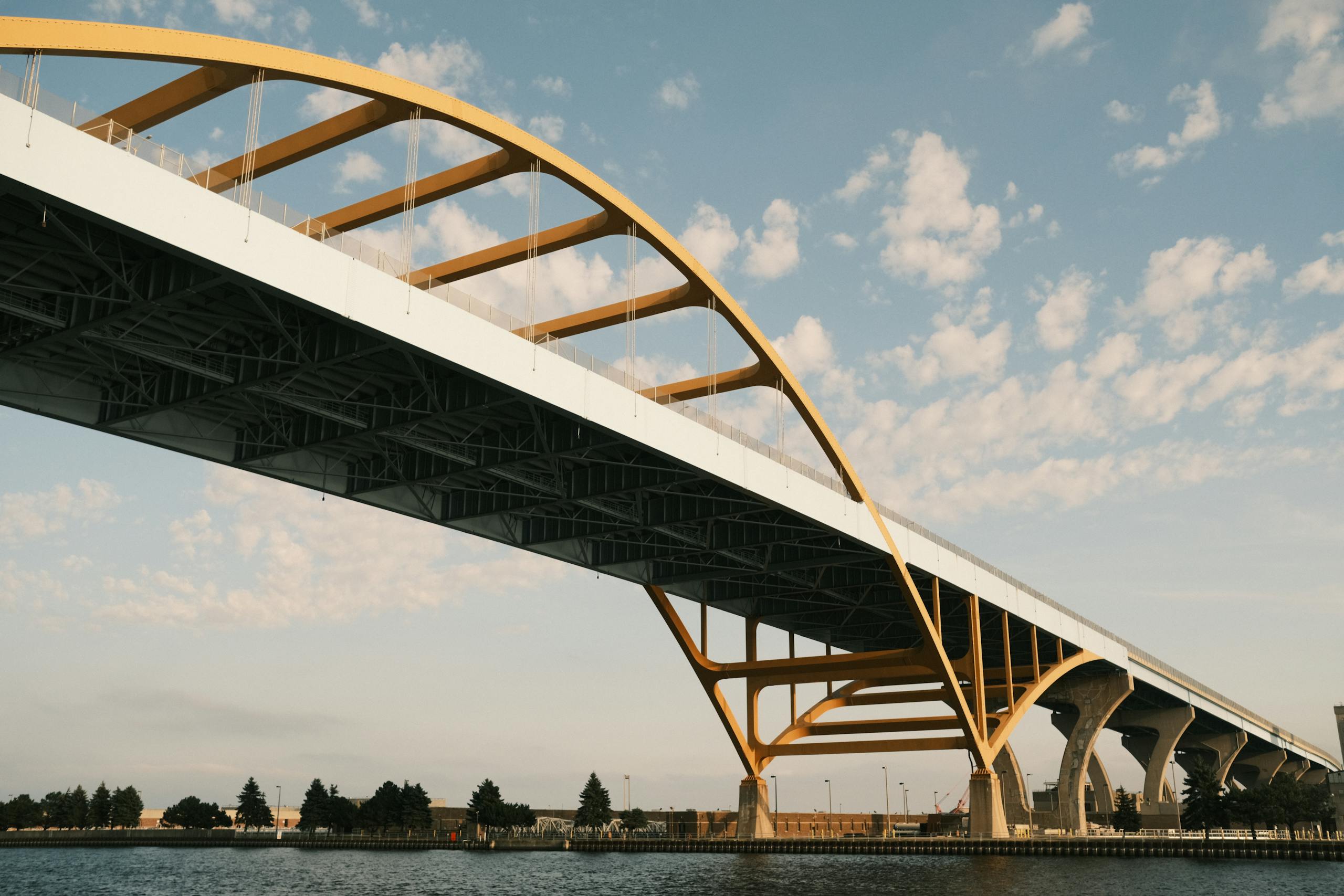 Wide-angle view of a modern bridge arching over a waterway under a clear blue sky.